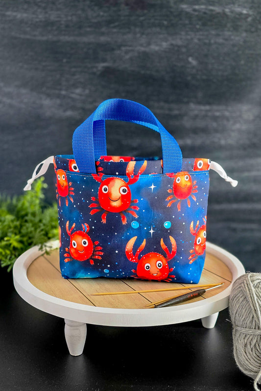 Projekttasche Crabby Galaxy aus Baumwolle mit Krabbenmotiv vor dunklem Hintergrund, ideal zum Stricken.