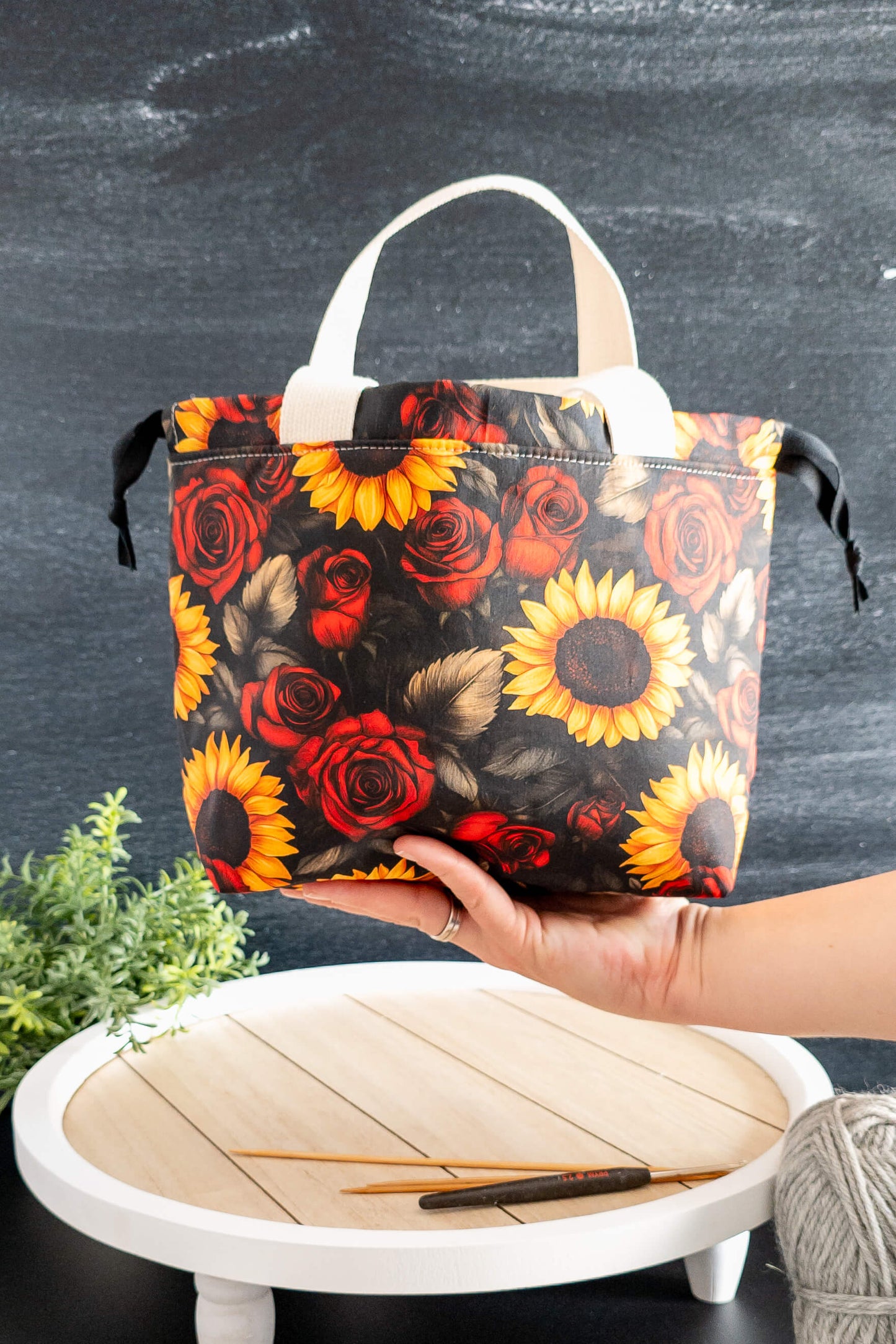 Golden Bloom als stilvolle Stricktasche auf einer weißen Holzplatte mit Strickzubehör
