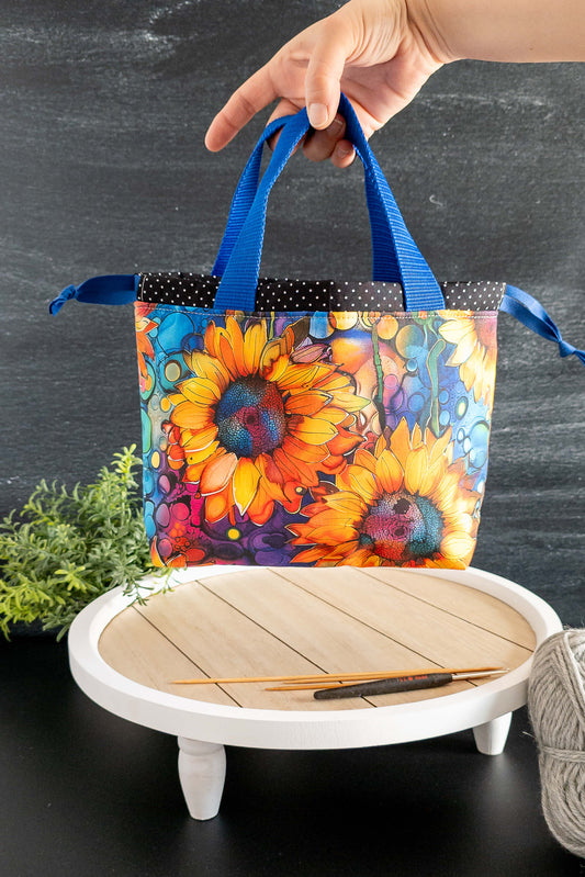 Projekttasche mit buntem Sonnenblumen-Print auf schwarzem Hintergrund, stehend auf weißem Tisch