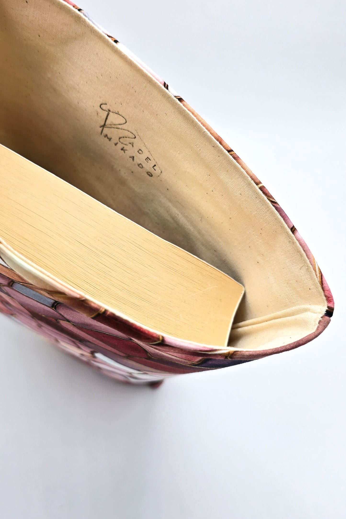 Stilvolle Buchhülle als Geschenkidee für Leseratten, dekorativ in Szene gesetzt mit Buch und Pflanzen im Hintergrund.