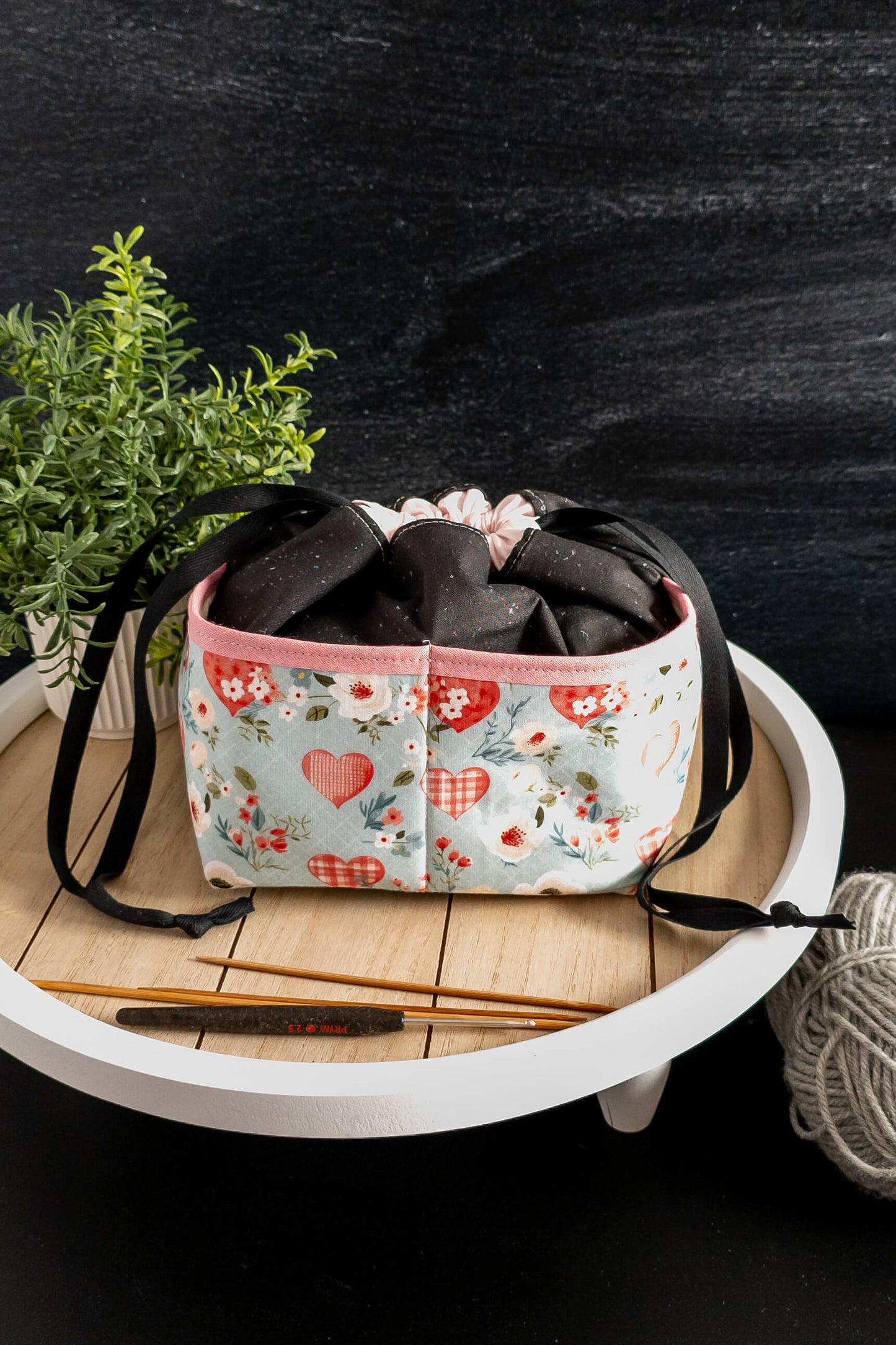Handarbeitstasche liebevoll platziert auf einem Tisch, mit Garnknäuel und Stricknadeln daneben.