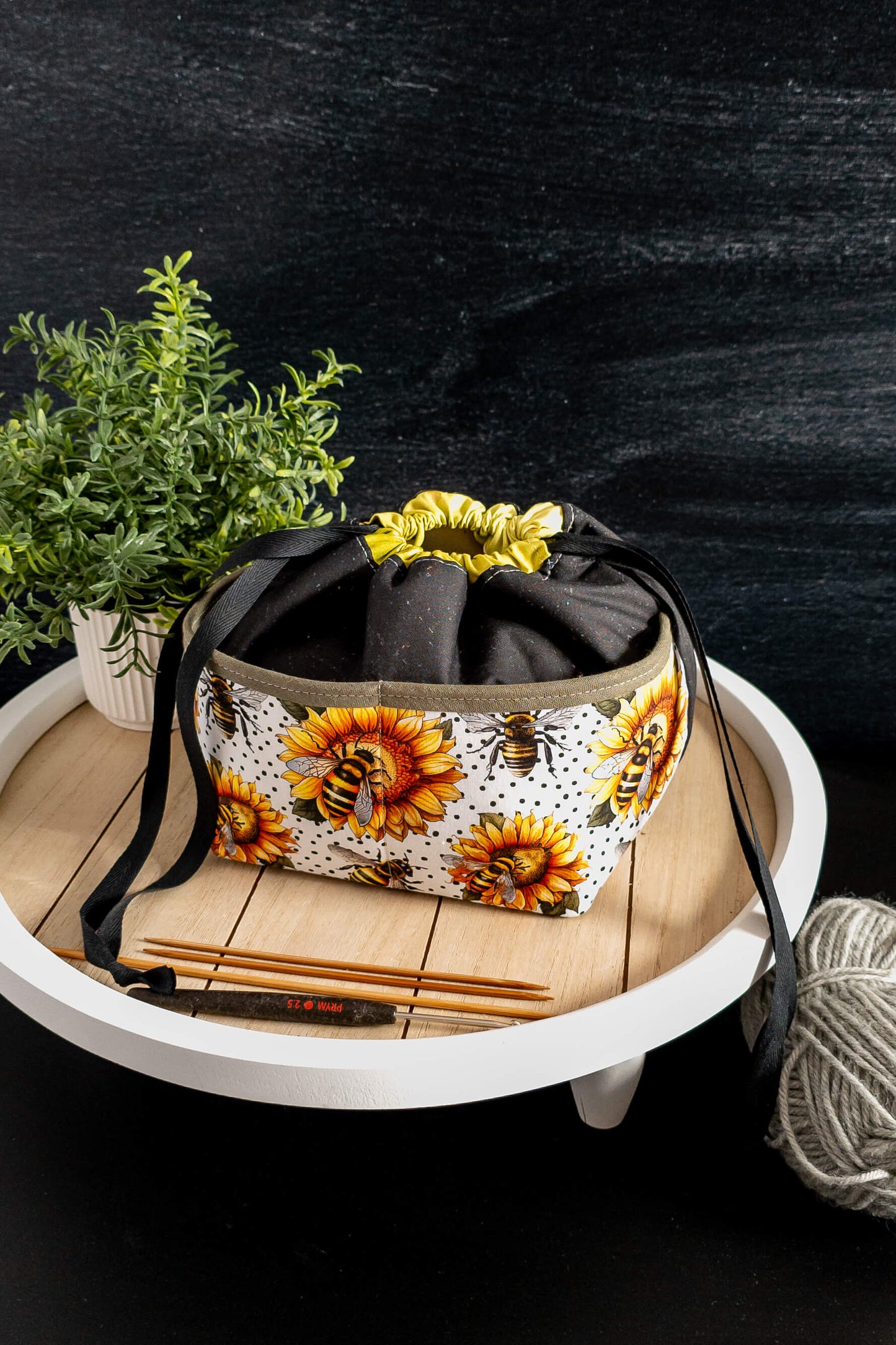Stricktasche „Sonnenzauber“ in der Natur, umgeben von grünen Pflanzen, harmoniert mit dem blumigen Design und strahlt sommerliche Leichtigkeit aus