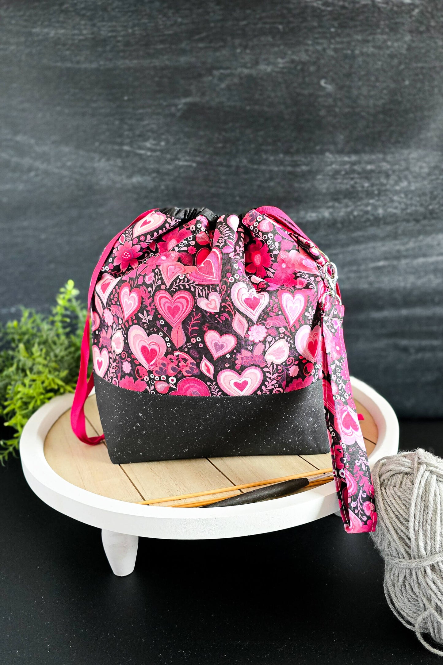 Handgenähte Projekttasche mit Herzmuster in Pink und Schwarz auf weißem Podest präsentiert