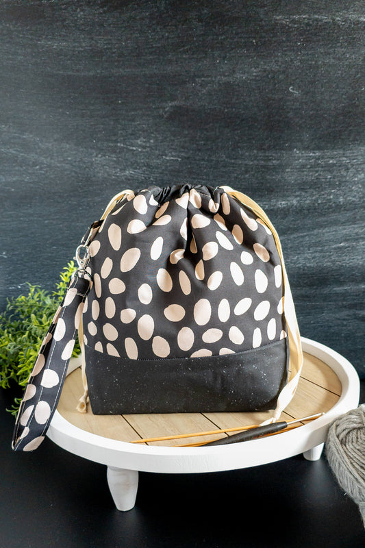 Handgenähte Projekttasche in Schwarz mit cremefarbenem Muster, stehend auf einem runden Tablett