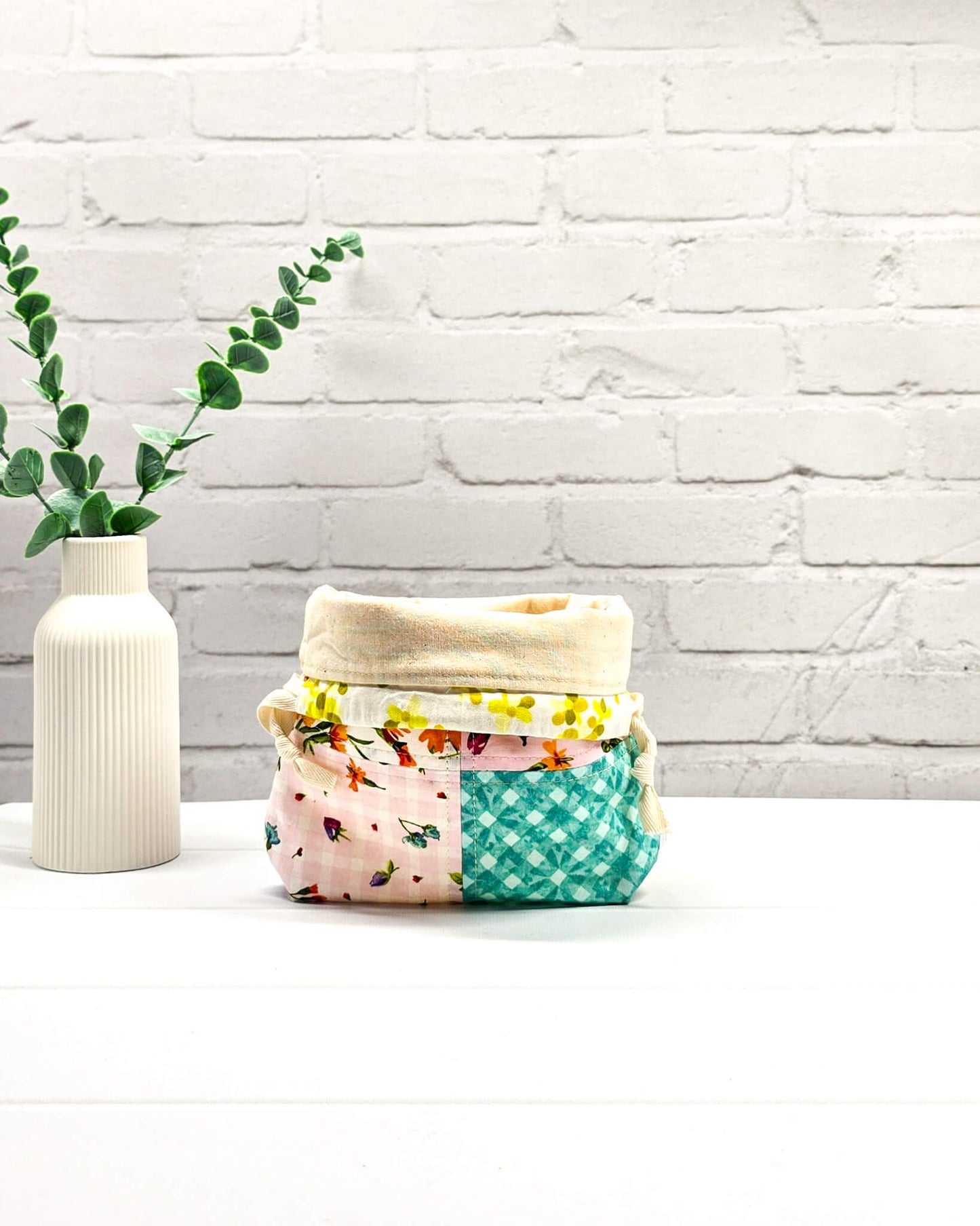 Kleine Projekttasche XS aus weißem Baumwollstoff mit einem bunten Blumen-Muster, einem schwarzen, weiß gepunkteten oberen Rand und schwarzen Kordelzügen. Handgenäht in Bayern von Nadelmikado.