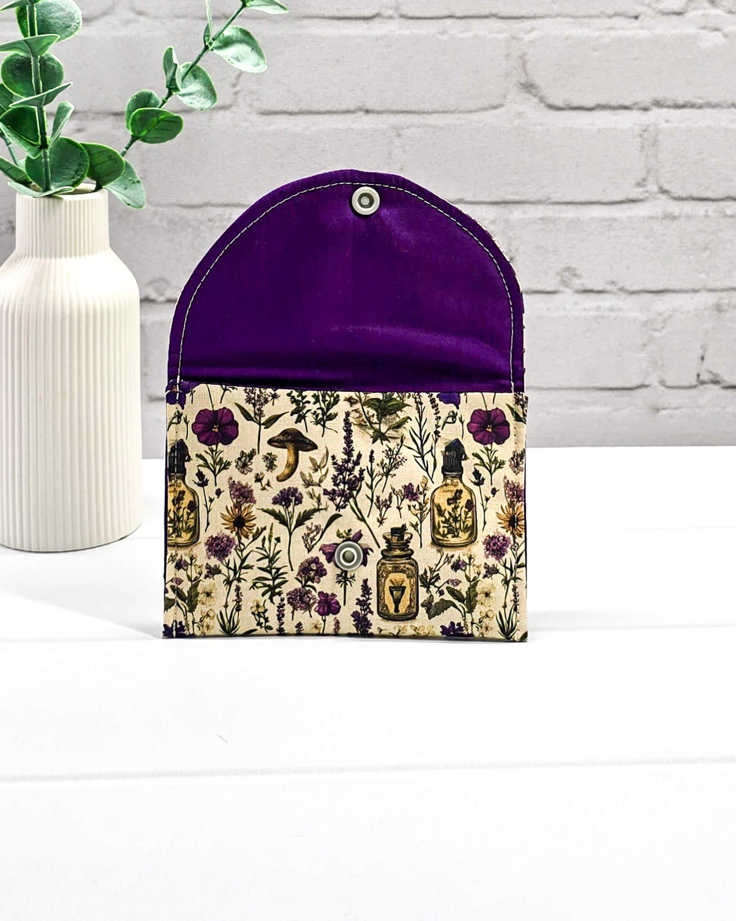 Kleine flache Zubehörtasche Mini Pouch mit abgerundeter Klappe, hellem Druckknopf und botanischem Kräuterküche-Muster auf beigem Grund. Handgenäht in Bayern von Nadelmikado.