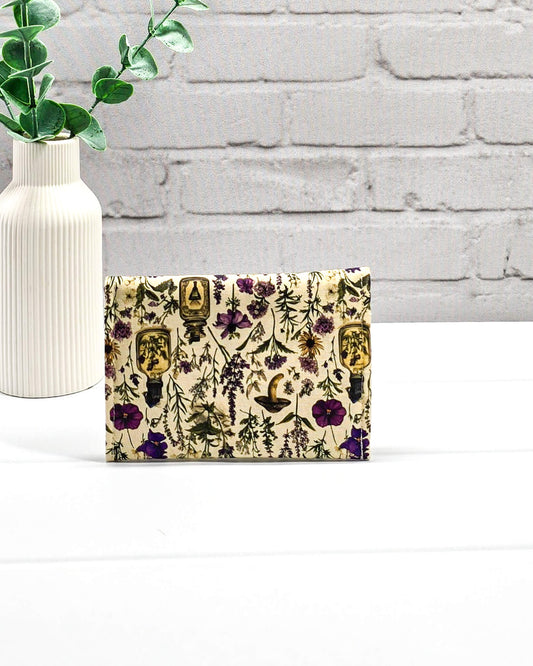 Kleine flache Zubehörtasche Mini Pouch mit abgerundeter Klappe, hellem Druckknopf und botanischem Kräuterküche-Muster auf beigem Grund. Handgenäht in Bayern von Nadelmikado.