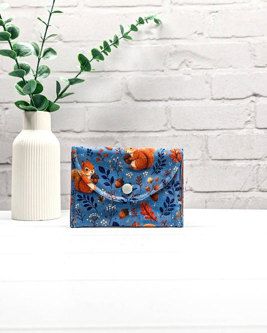 Mini Pouch für Strickzubehör aus blauem Baumwollstoff mit orangefarbenen Eichhörnchen und Eicheln, orangefarbener Klappe und Druckknopf. Handgenäht in Bayern von Nadelmikado.