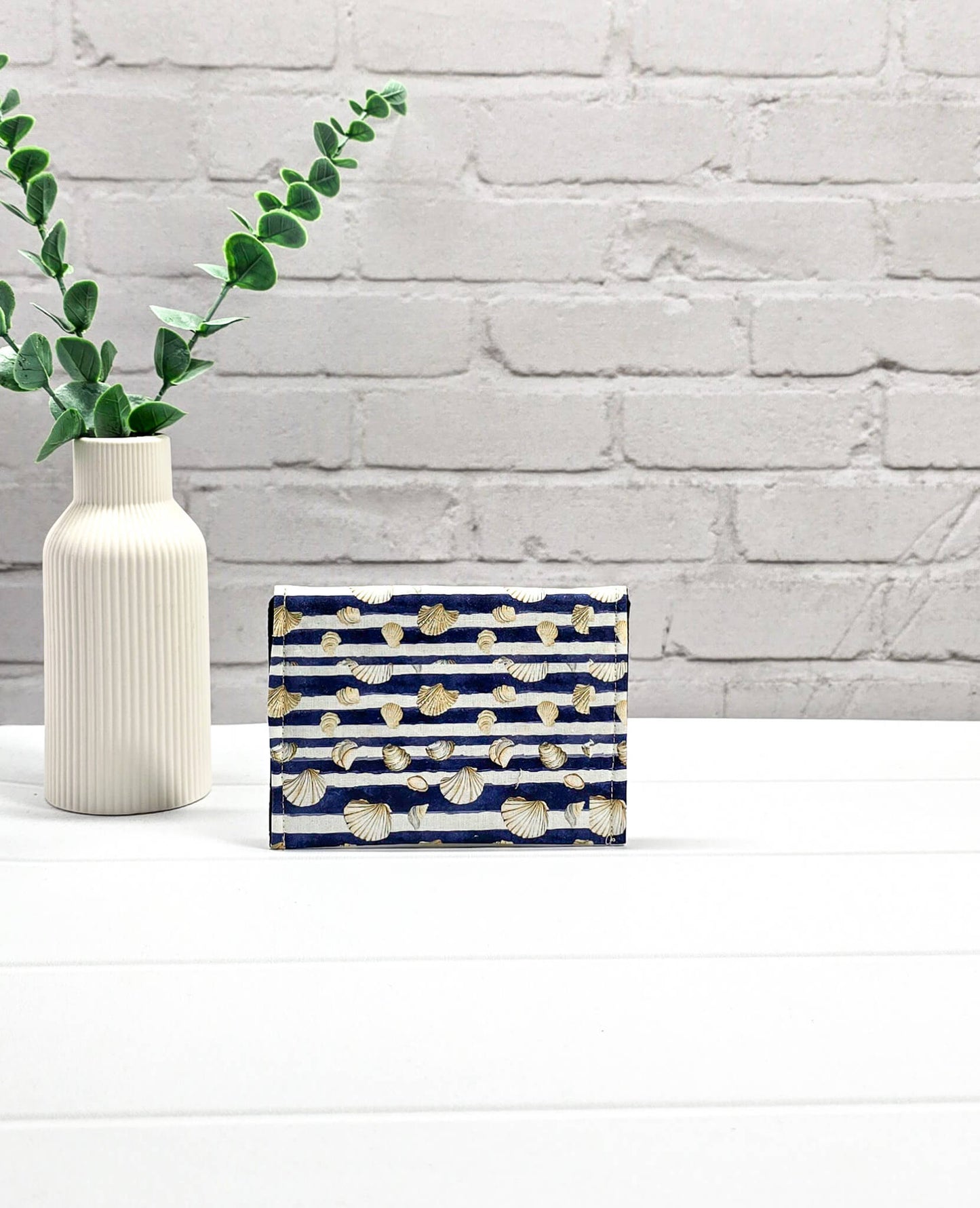 Kleine Mini Pouch aus blau-weiß quergestreiftem Stoff mit kleinen Muschelmotiven und einem hellgrauen Druckknopf auf der geschwungenen Klappe. Handgenäht in Bayern von Nadelmikado.