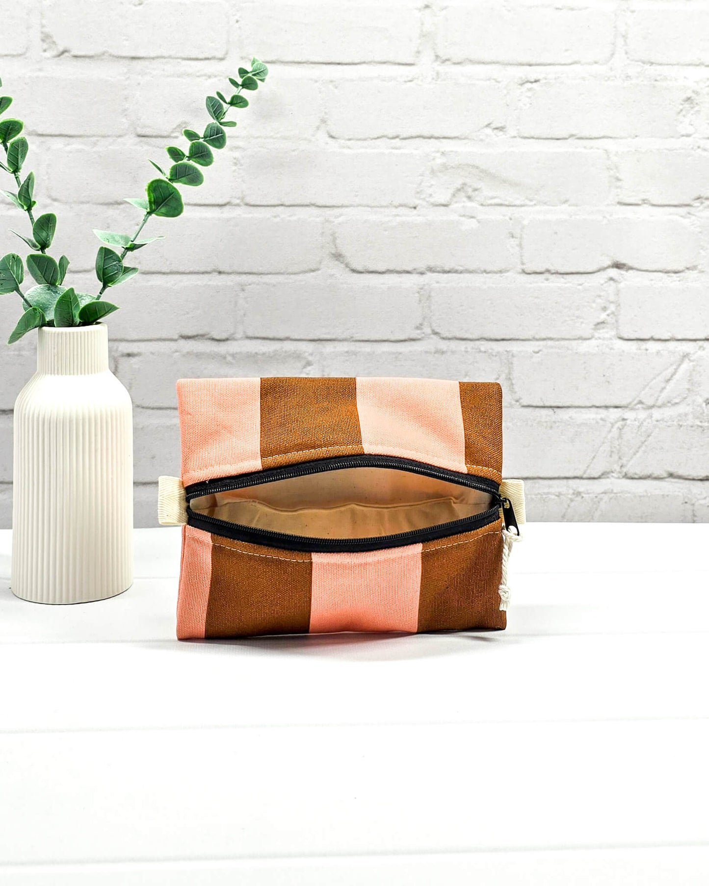 Mini Zip Pouch mit breiten vertikalen Streifen in Braun und Rosa, einem schwarzen, mittigen Reißverschluss und hellen Stofflaschen. Handgenäht in Bayern von Nadelmikado.