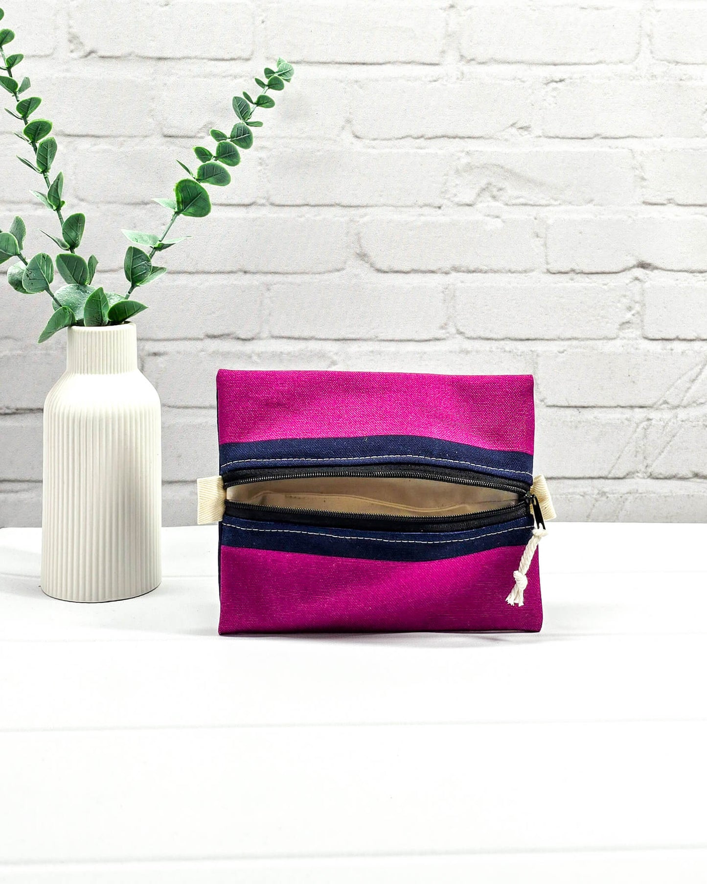 Mini Zip Pouch mit breiten horizontalen Streifen in Fuchsia und Dunkelblau, einem schwarzen mittigen Reißverschluss und hellen Stofflaschen. Handgenäht in Bayern von Nadelmikado.