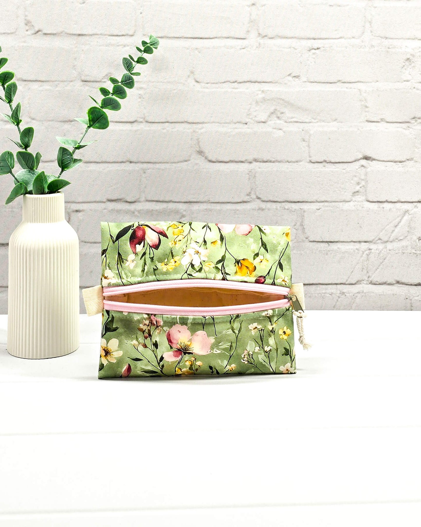 Mini Zip Pouch mit einem floralen Muster auf olivgrünem Stoff, einem rosafarbenen mittigen Reißverschluss und hellen Stofflaschen. Handgenäht in Bayern von Nadelmikado.