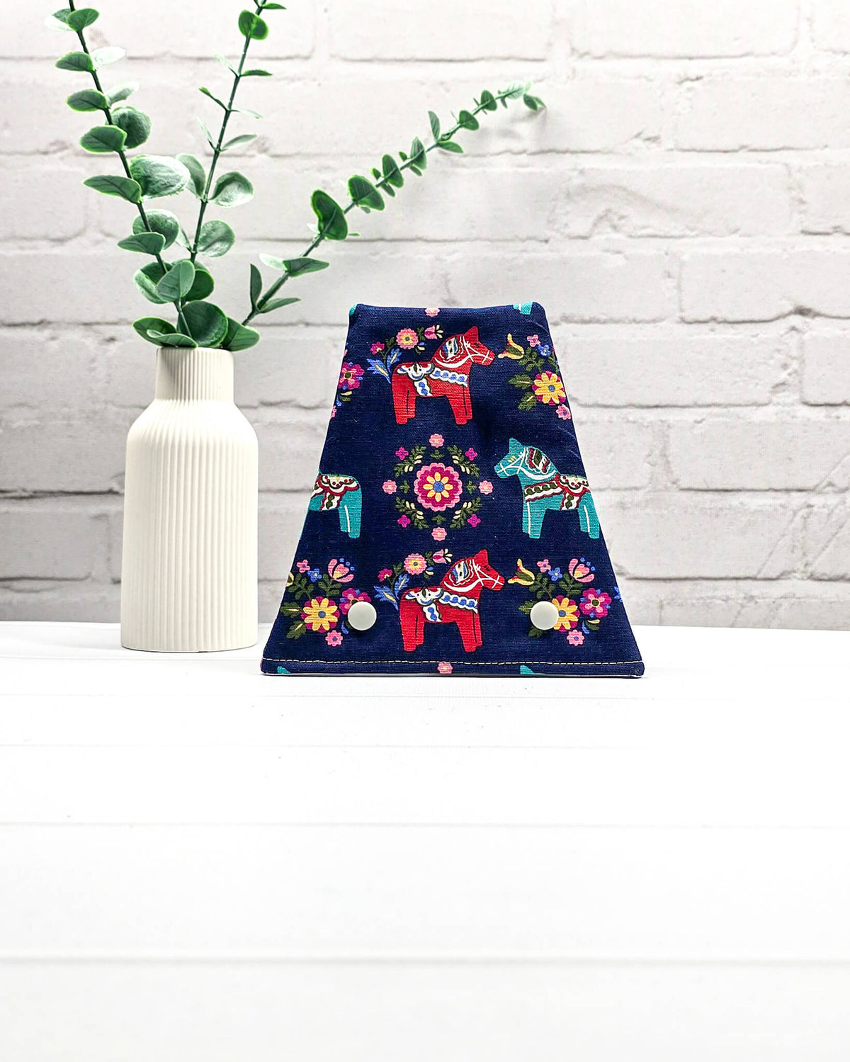 Nadelgarage für Trio-Stricknadeln aus dunkelblauem Stoff mit bunten Dala-Pferden, Blumenmotiven und zwei hellen Druckknöpfen. Handgenäht in Bayern von Nadelmikado.