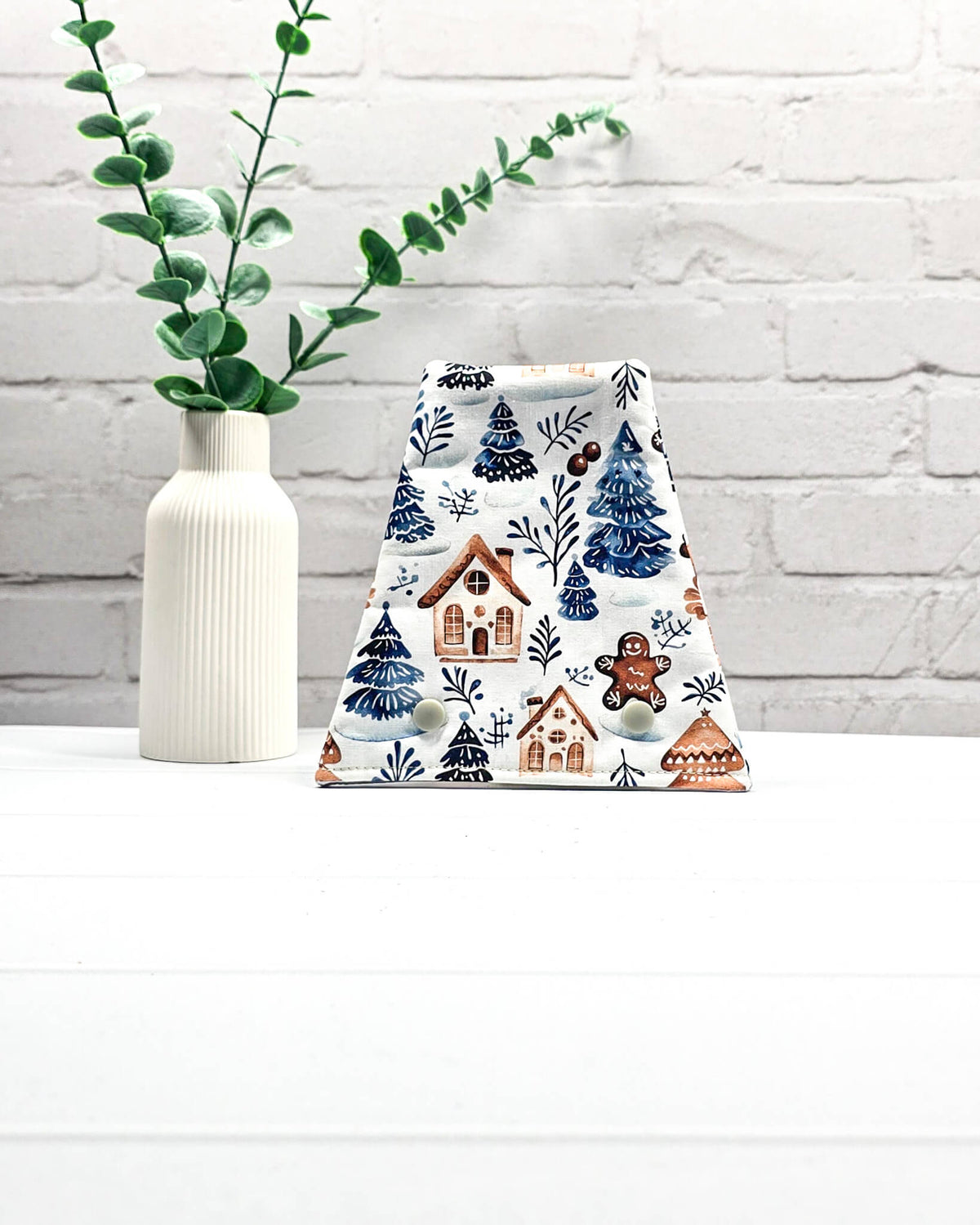 Nadelgarage für Trio-Stricknadeln aus weißem Stoff mit blauen Tannenbäumen, kleinen Häusern, Lebkuchenfigur und zwei hellen Druckknöpfen. Handgenäht in Bayern von Nadelmikado.