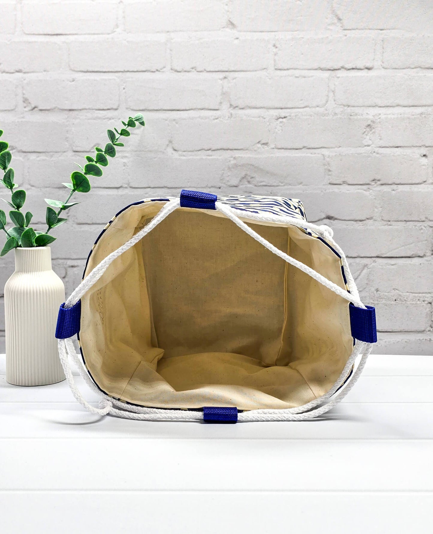 Projektbeutel Aska M aus blau-weiß quergestreiftem Stoff mit kleinen Muschelmotiven, zwei seitlich herausgeführten, hellen Kordeln und einer blauen Schlaufe an der Oberkante. Rice Bag. Handgenäht in Bayern von Nadelmikado.