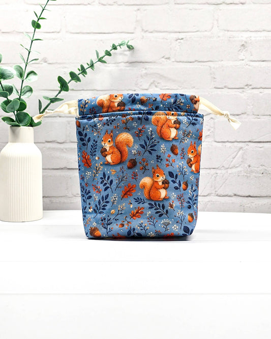 Kleiner Projektbeutel Tindra mit Tunnelzug aus blauem Baumwollstoff mit orangefarbenen Eichhörnchen, Eicheln und Blättern für Strickprojekte bis 50 g Wolle. Handgenäht in Bayern von Nadelmikado.