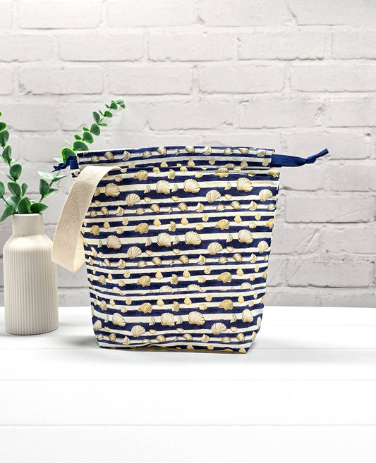Projektbeutel Tuva S aus blau-weiß quergestreiftem Stoff mit kleinen Muschelmotiven, einer hellen Gurtband-Schlaufe und dunkelblauem Kordelzug. Handgenäht in Bayern von Nadelmikado.