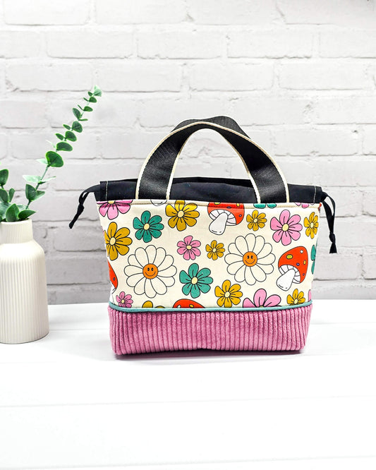 Handgemachte Projekttasche Alva in Größe S mit zwei Tragegriffen, bunten Retro-Pilzen und Blumen auf hellem Stoff und einem Taschenboden aus altrosa Breitcord. Handgenäht in Bayern von Nadelmikado.