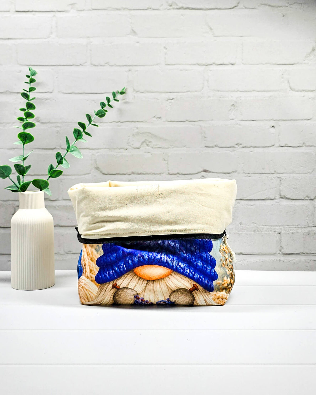 Projektbeutel Größe M mit Wichtel, blauer Mütze und blauem Strickzeug auf hellem Grund sowie schwarzem Reißverschluss. Handgenäht in Bayern von Nadelmikado.