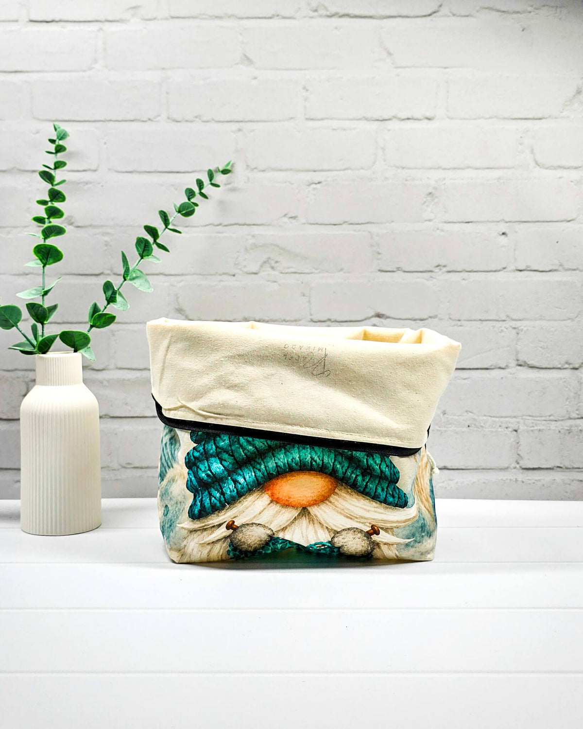 Projektbeutel Größe M mit Wichtel, türkiser Mütze und türkisem Strickzeug auf hellem Grund sowie schwarzem Reißverschluss. Handgenäht in Bayern von Nadelmikado.