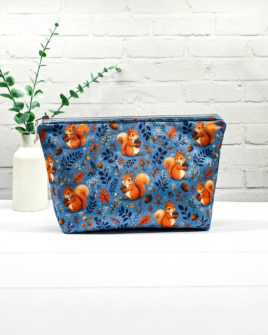 Kleine Projekttasche mit Reißverschluss aus blauem Baumwollstoff mit orangefarbenen Eichhörnchen, Eicheln und Blättern. Handgenäht in Bayern von Nadelmikado.