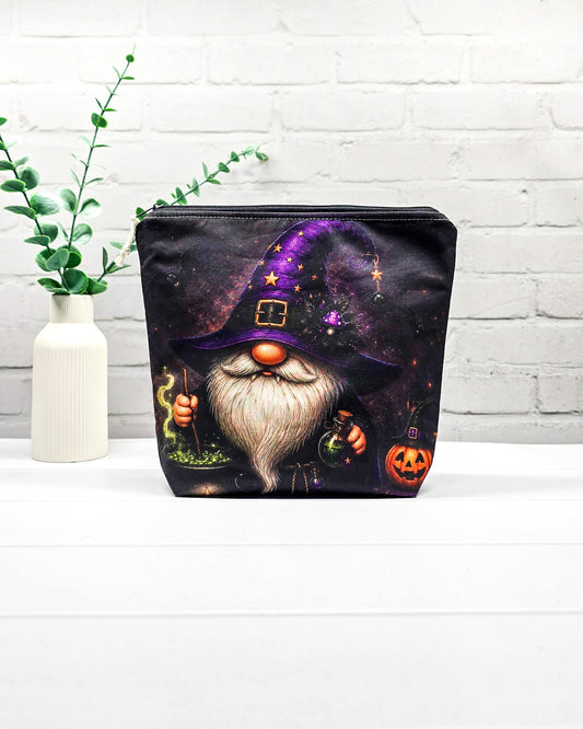 Projekttasche Isvind Größe S mit Halloweenwichtel, lila Hexenhut, weißem Bart, grün blubberndem Zaubertrank und orangefarbenem Kürbis auf dunklem Stoff. Mit Reißverschluss für kleine Strickprojekte. Handgenäht in Bayern von Nadelmikado.