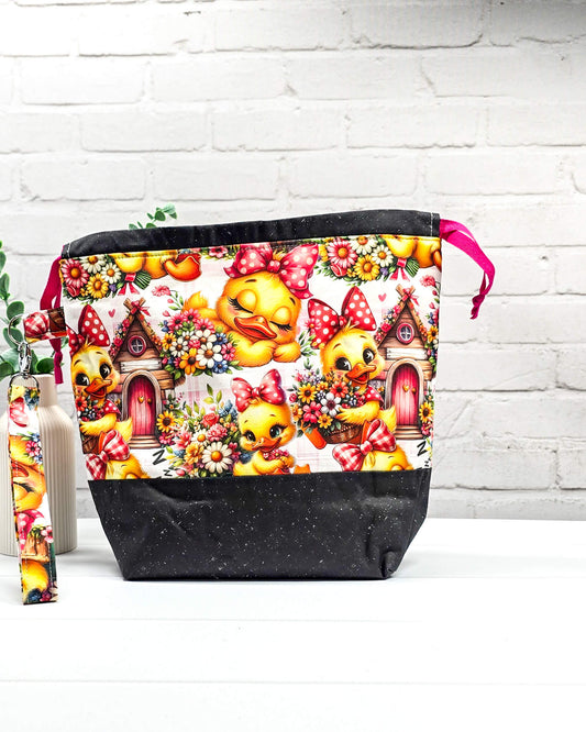 Projekttasche Tuva M aus Baumwolle mit gelben Küken, Blumenmotiven, pinken Zugkordeln und abnehmbarer Handschlaufe. Handgenäht in Bayern von Nadelmikado.