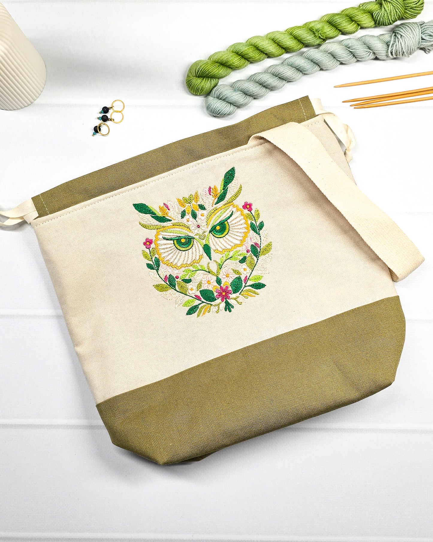 Projekttasche Tuva M aus hellem Canvas mit gesticktem Eulenmotiv, olivgrünem Boden, Kordelzug und Tragegurt. Bietet Platz für 400g Wolle. Handgenäht in Bayern von Nadelmikado.