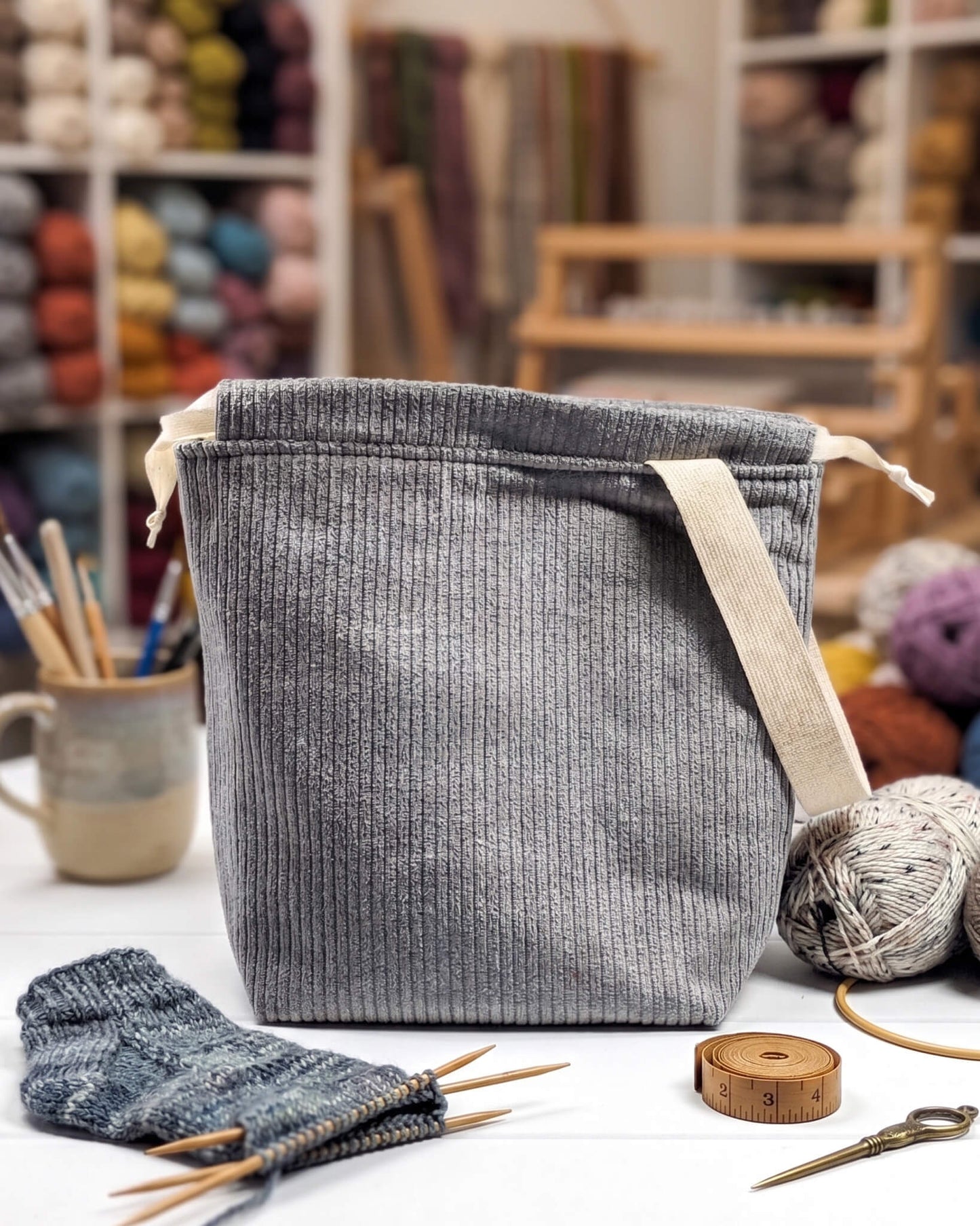 Graue Projekttasche Tuva M aus Cordstoff mit einem hellen Gurtband-Henkel an der Seite und cremefarbenen Kordeln, handgenäht von Nadelmikado in Bayern.