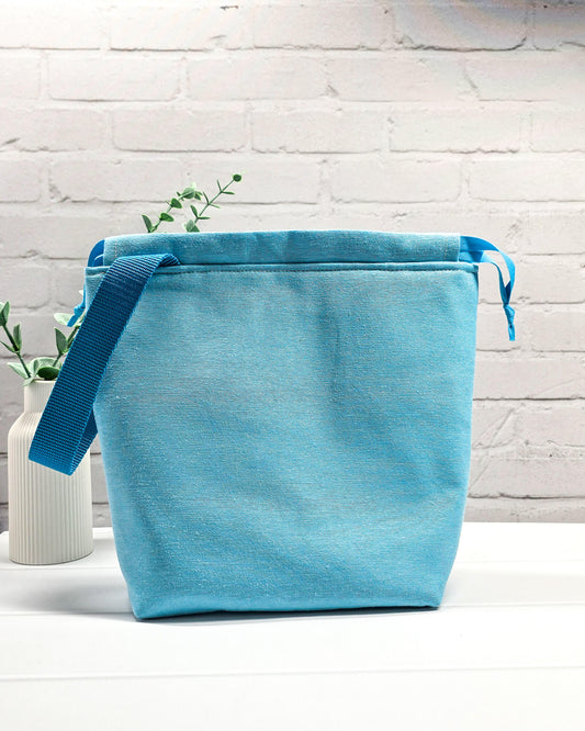 Projekttasche Tuva M aus hellem Canvas und hellblauem Stoff mit blau gesticktem Seepferdchen-Motiv im Korallenkranz, Kordelzug und blauem Tragegurt. Bietet Platz für 400g Wolle und schützt das Strickzeug vor Verheddern. Handgenäht in Bayern von Nadelmikado.