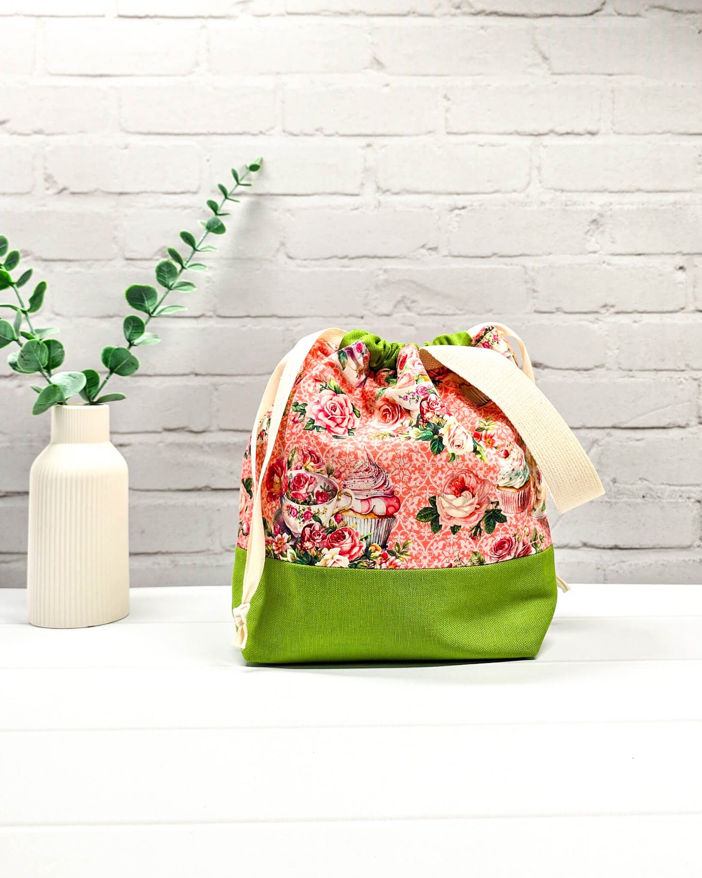 Handgenähter Projektbeutel mit Rosen- und Teetassen-Motiv auf rosa Mustergrund, grünem Boden, cremefarbenem Kordelzug und Tragegurt. Für 200g Wolle. Handgenäht in Bayern von Nadelmikado.