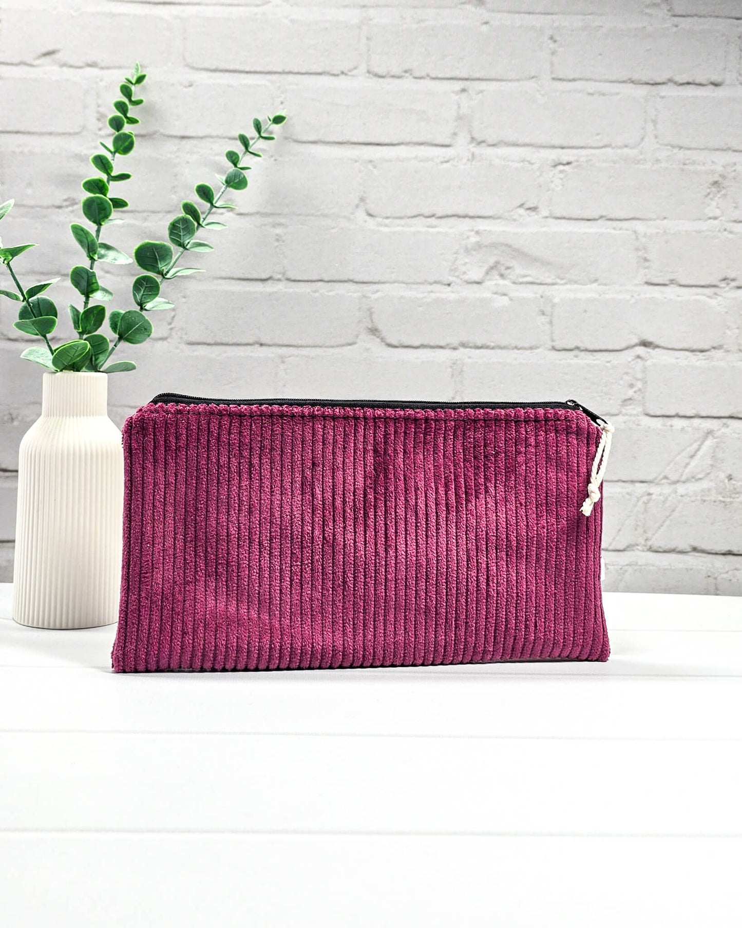 Kleine Reißverschlusstasche aus beerenfarbenem Cord-Stoff auf hellem Untergrund mit Strickzubehör. Handgenäht in Bayern von Nadelmikado.