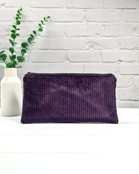 Kleine lila Reißverschlusstasche aus Cord-Stoff für Strickzubehör, flach liegend auf weißem Untergrund mit einer Schere, Garnsträngen und Holznadeln. Handgenäht in Bayern von Nadelmikado.