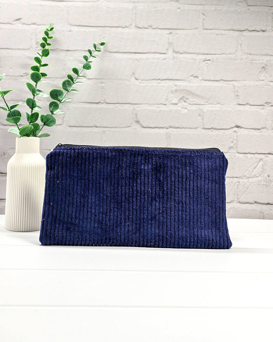 Kleine navyblaue Reißverschlusstasche aus Cord-Stoff für Strickzubehör, liegend auf weißem Untergrund mit einer Schere, Garnsträngen und Holznadeln. Handgenäht in Bayern von Nadelmikado.
