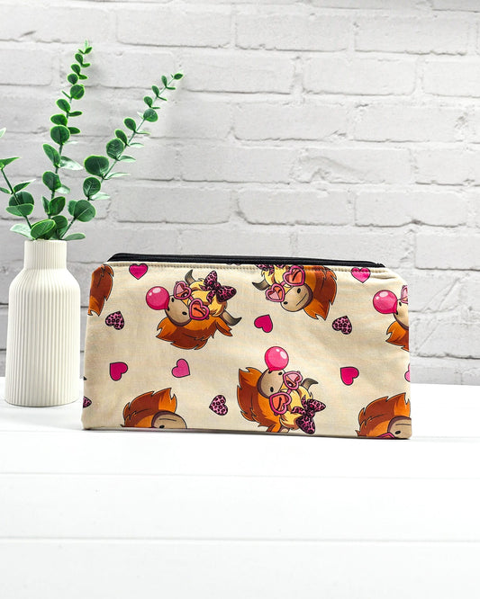 Längliche Tasche mit schwarzem Reißverschluss, hellem Kordel-Zipper und lustigem Highland-Cattle-Motiv mit Herzbrillen auf beigem Stoff. Handgenäht in Bayern von Nadelmikado.