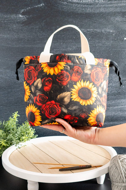 Golden Bloom als stilvolle Stricktasche auf einer weißen Holzplatte mit Strickzubehör