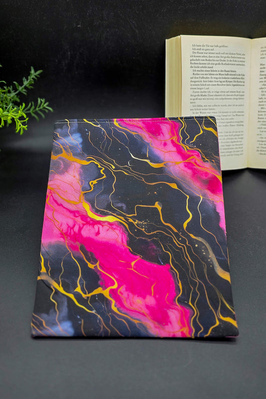 Handgemachte Buchhülle mit galaktischem Muster in Schwarz, Pink und Gold, liegend auf dunklem Hintergrund