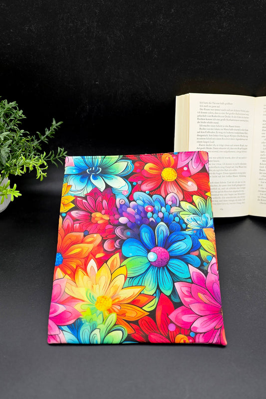 Handgemachte Buchhülle mit buntem Hippie-Blumenmuster, liegend auf schwarzem Hintergrund mit offenem Buch.