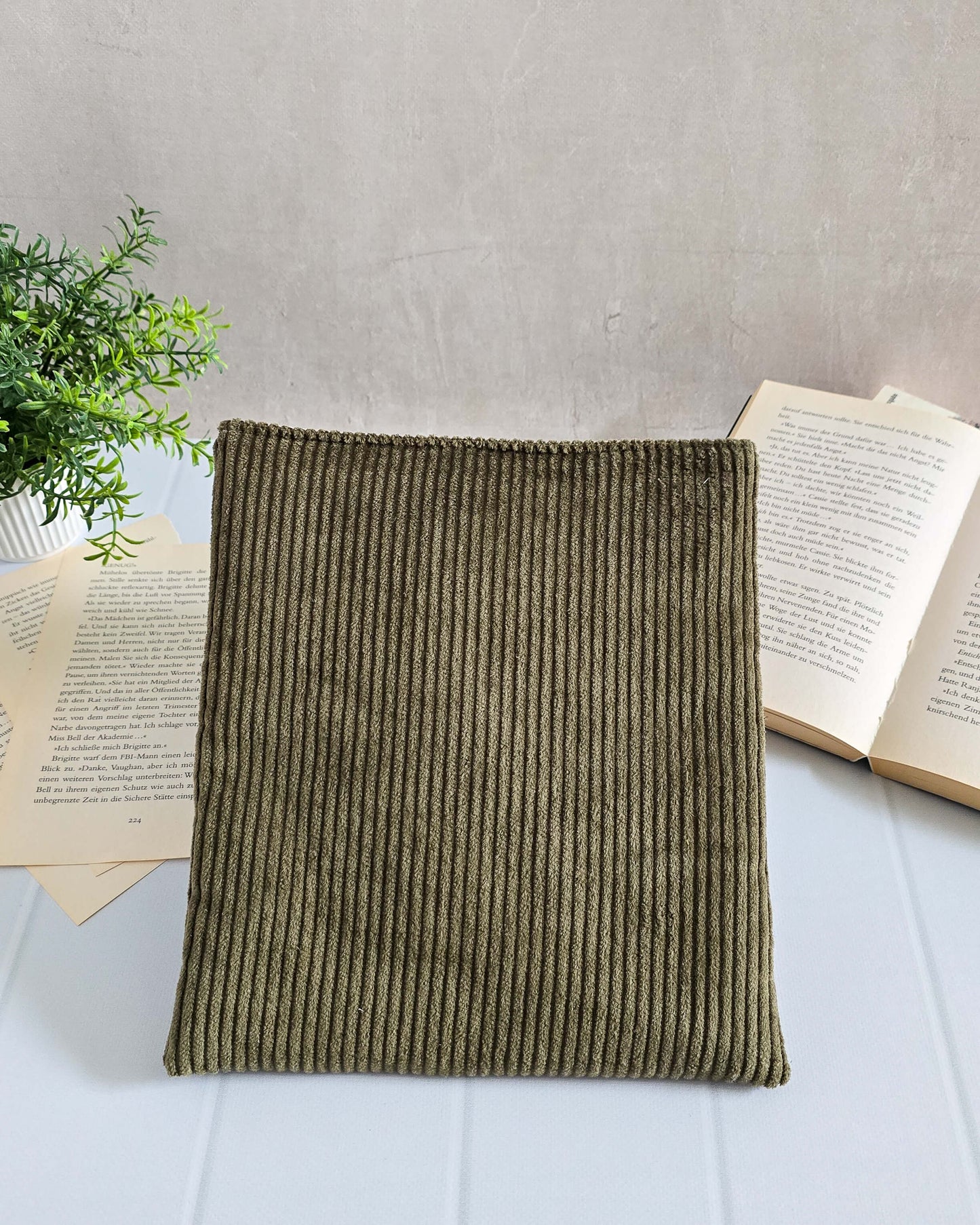 Olivgrüne Buchhülle aus Cordstoff, frontal vor aufgeschlagenem Buch fotografiert