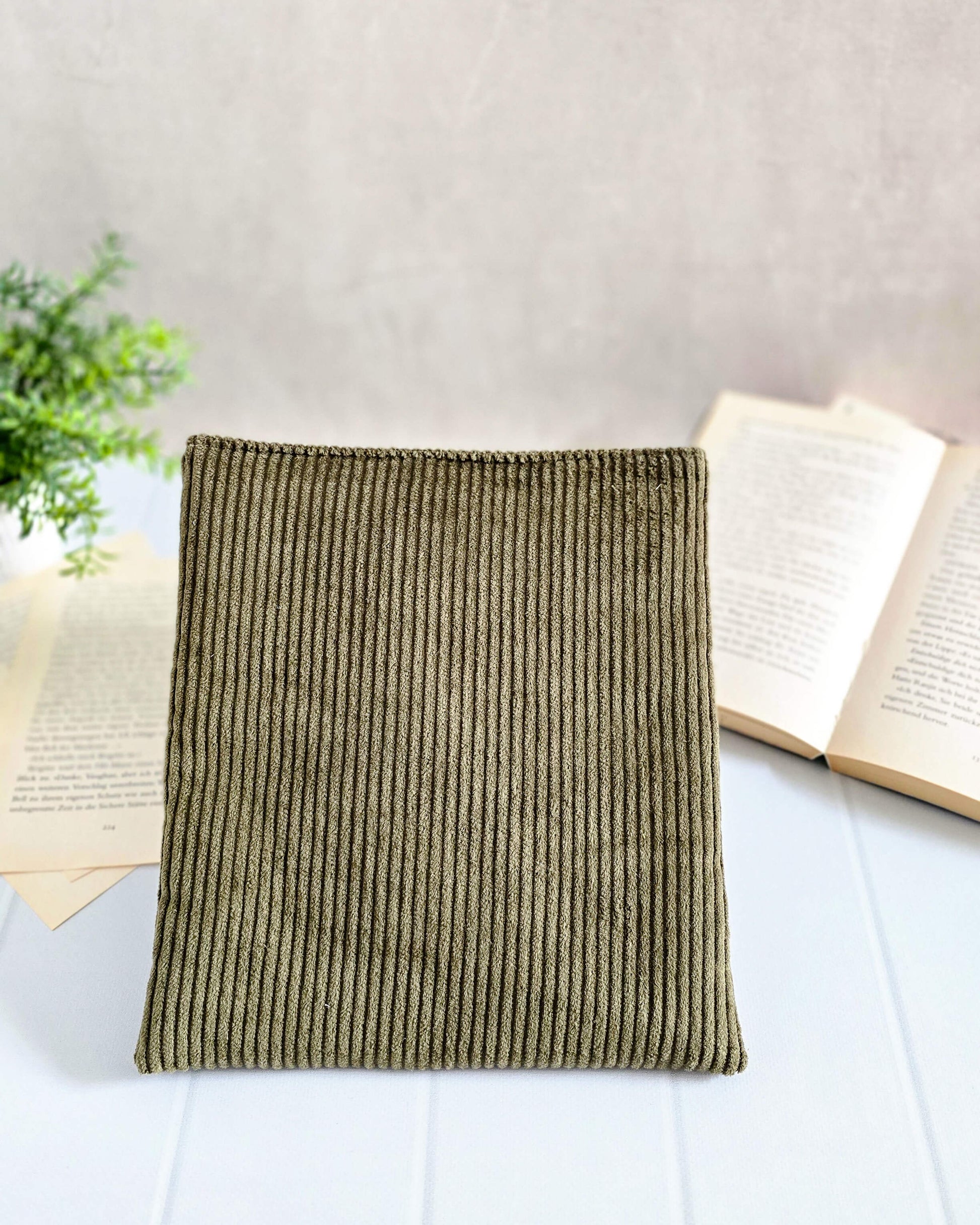 Olivgrüne Buchhülle aus Cordstoff, frontal vor aufgeschlagenem Buch fotografiert