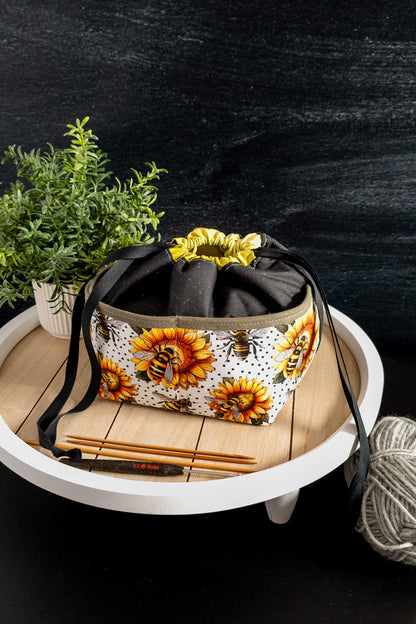 Stricktasche „Sonnenzauber“ in der Natur, umgeben von grünen Pflanzen, harmoniert mit dem blumigen Design und strahlt sommerliche Leichtigkeit aus
