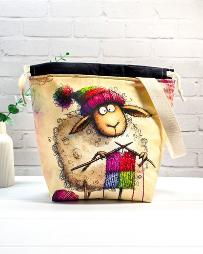 Stricktasche mit strickendem Schaf, bunter Mütze, Stricknadeln und Wollknäuel auf hellem Grund, handgenäht in Bayern von NadelMikado.