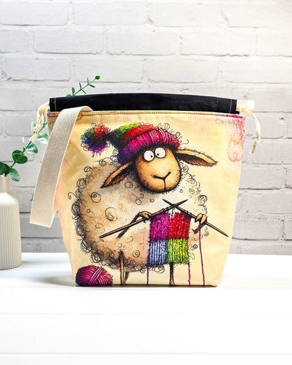Stricktasche mit strickendem Schaf, bunter Mütze, Stricknadeln und Wollknäuel auf hellem Grund, handgenäht in Bayern von NadelMikado.