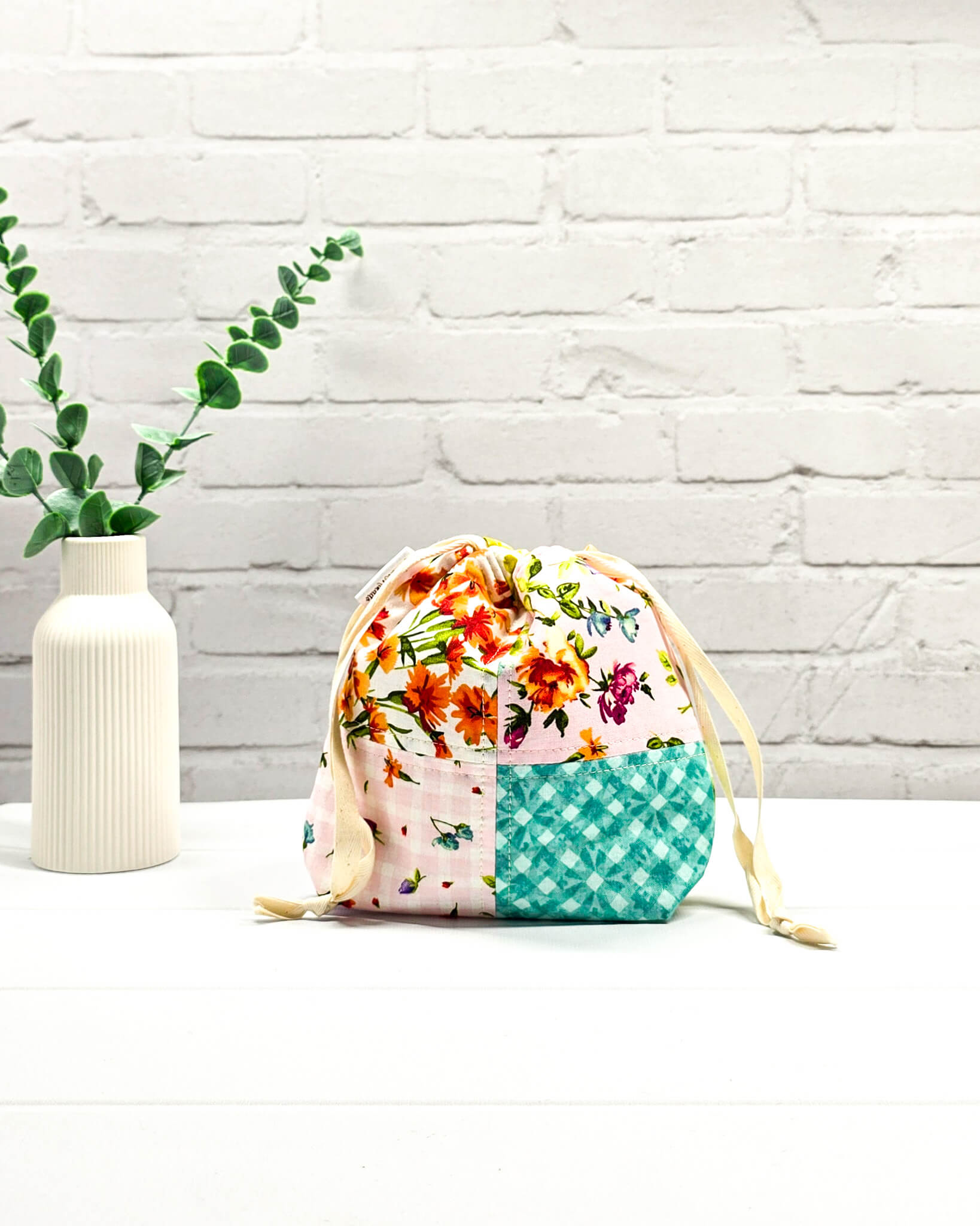 Kleine Projekttasche XS aus weißem Baumwollstoff mit einem bunten Blumen-Muster, einem schwarzen, weiß gepunkteten oberen Rand und schwarzen Kordelzügen. Handgenäht in Bayern von Nadelmikado. 