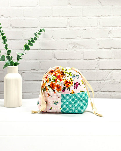 Kleine Projekttasche XS aus weißem Baumwollstoff mit einem bunten Blumen-Muster, einem schwarzen, weiß gepunkteten oberen Rand und schwarzen Kordelzügen. Handgenäht in Bayern von Nadelmikado. 