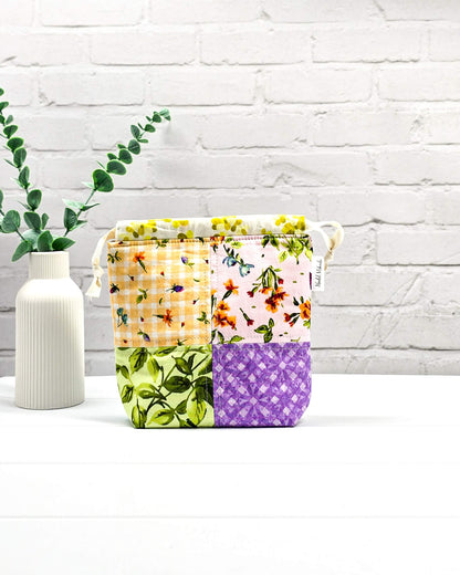 Kleine Projekttasche XS aus weißem Baumwollstoff mit einem bunten Blumen-Muster, einem schwarzen, weiß gepunkteten oberen Rand und schwarzen Kordelzügen. Handgenäht in Bayern von Nadelmikado. 