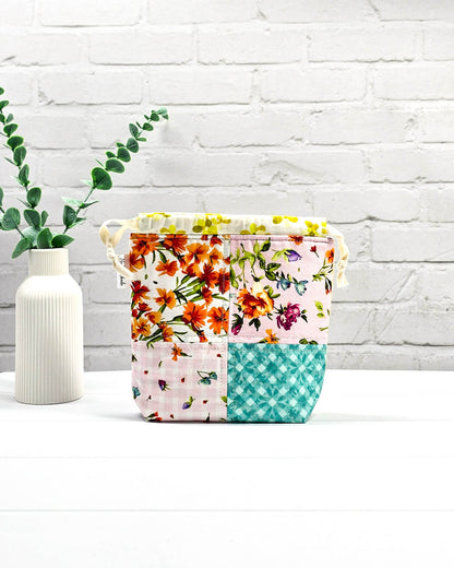 Kleine Projekttasche XS aus weißem Baumwollstoff mit einem bunten Blumen-Muster, einem schwarzen, weiß gepunkteten oberen Rand und schwarzen Kordelzügen. Handgenäht in Bayern von Nadelmikado. 