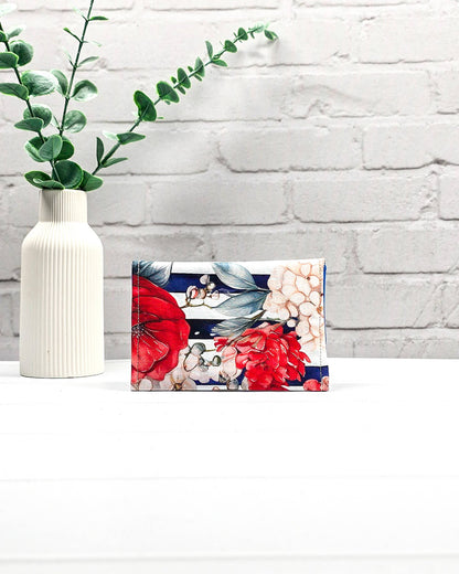 Mini Pouch mit roten und cremefarbenen Blüten auf dunkelblau-weiß gestreiftem Stoff, leuchtend blauer Innenklappe und schwarzen Druckknöpfen. Kleine Zubehörtasche für Maschenmarkierer und Strickzubehör. Handgenäht in Bayern von NadelMikado.