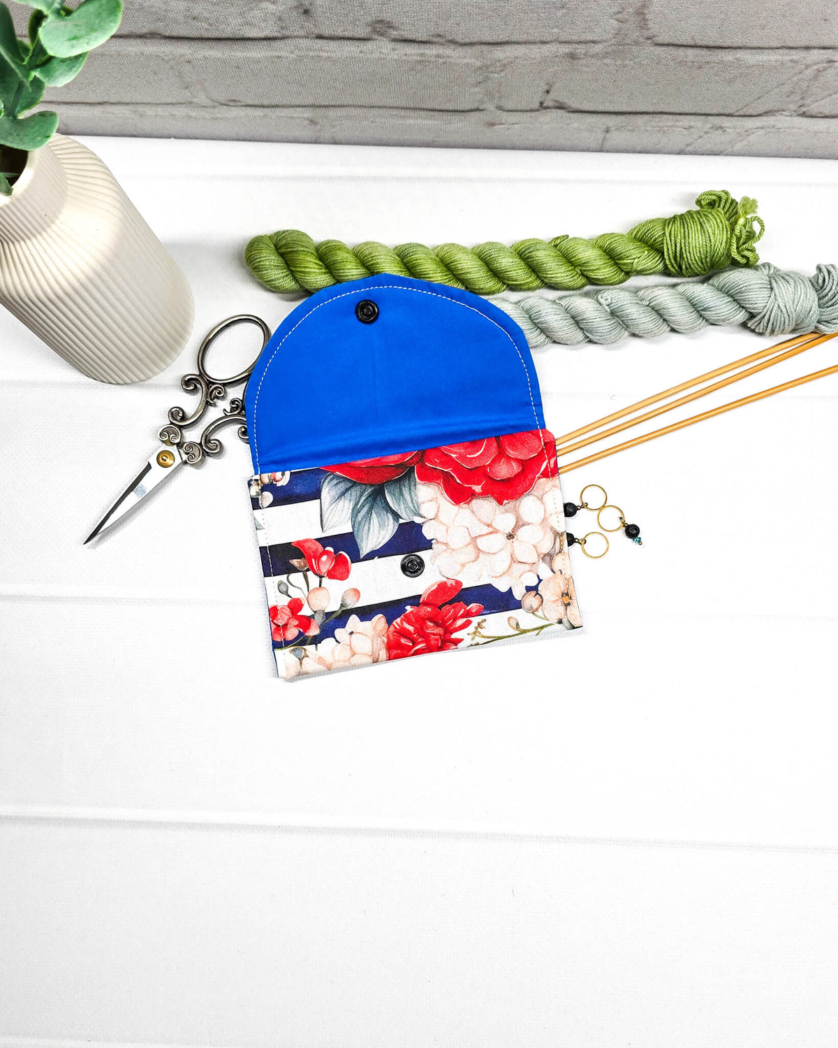 Mini Pouch mit roten und cremefarbenen Blüten auf dunkelblau-weiß gestreiftem Stoff, leuchtend blauer Innenklappe und schwarzen Druckknöpfen. Kleine Zubehörtasche für Maschenmarkierer und Strickzubehör. Handgenäht in Bayern von NadelMikado.