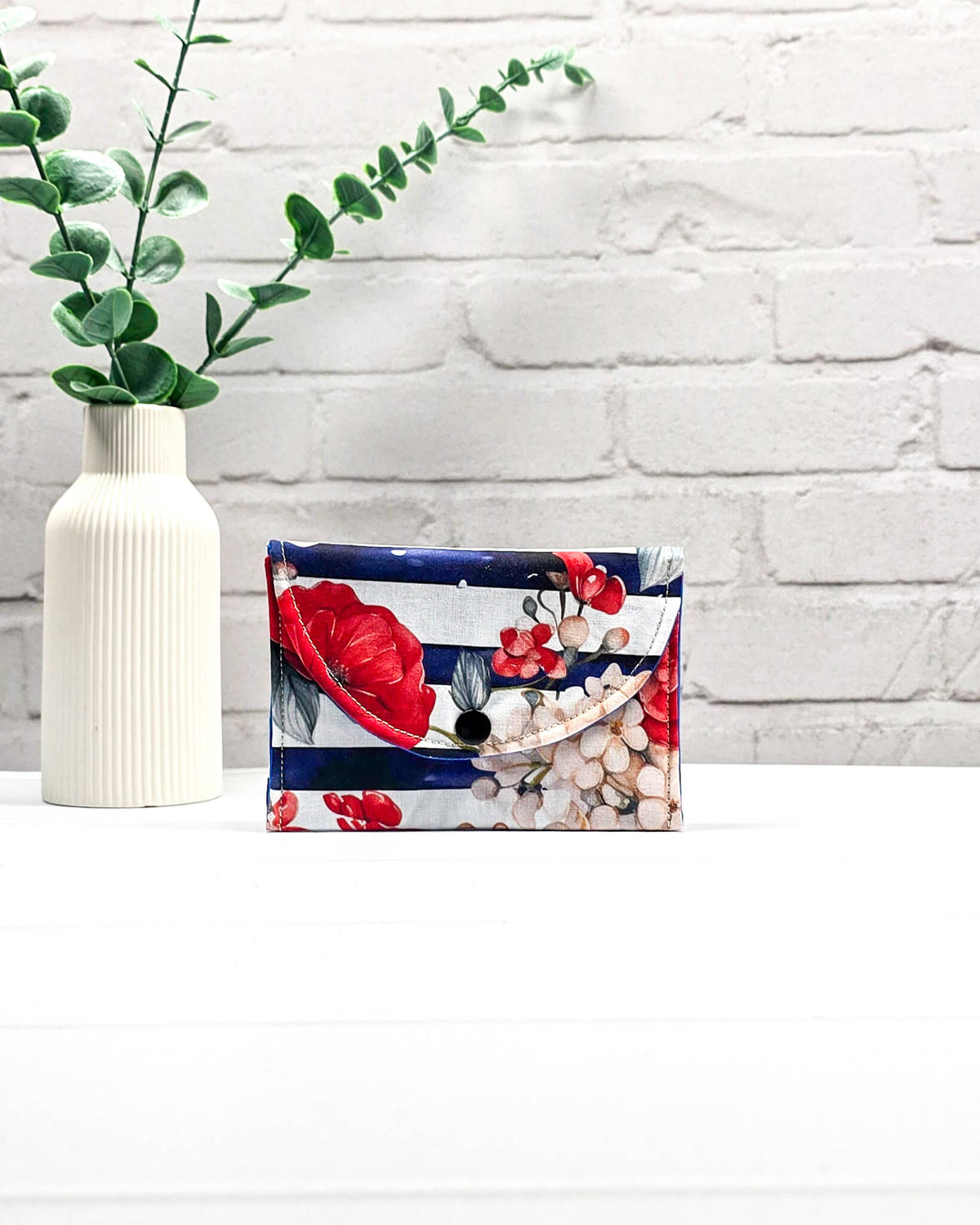 Mini Pouch mit roten und cremefarbenen Blüten auf dunkelblau-weiß gestreiftem Stoff, leuchtend blauer Innenklappe und schwarzen Druckknöpfen. Kleine Zubehörtasche für Maschenmarkierer und Strickzubehör. Handgenäht in Bayern von NadelMikado.